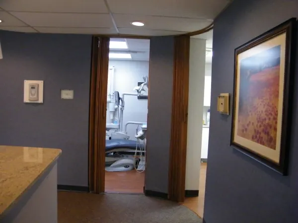 A corridor with framed art, looking into a treatment room with a dental chair.