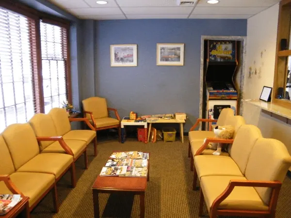 The waiting room at Comprehensive Dental Group: yellow armchairs, a coffee table and a children&rsquo;s arcade cabinet.