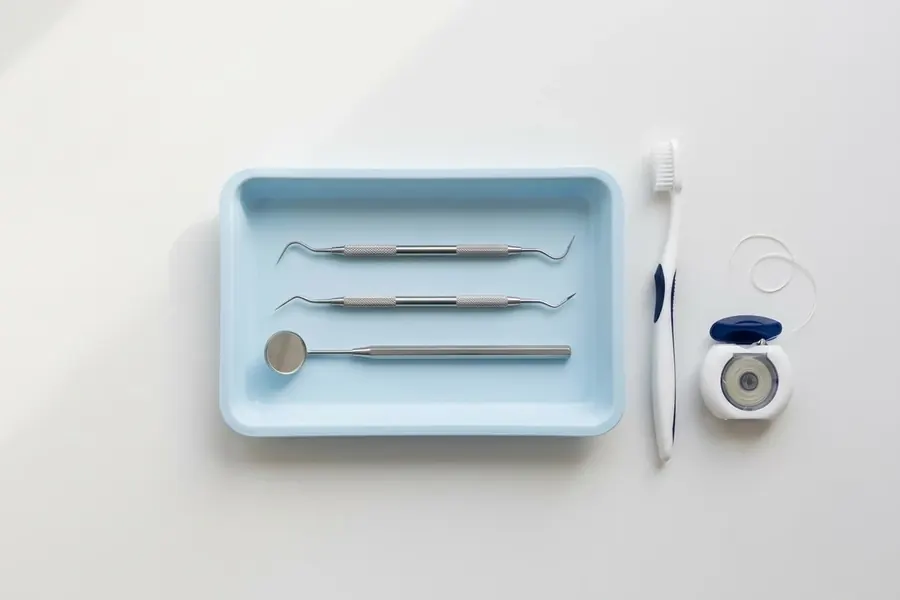 A dental mirror, scaler and explorer on a blue tray beside a toothbrush and floss.